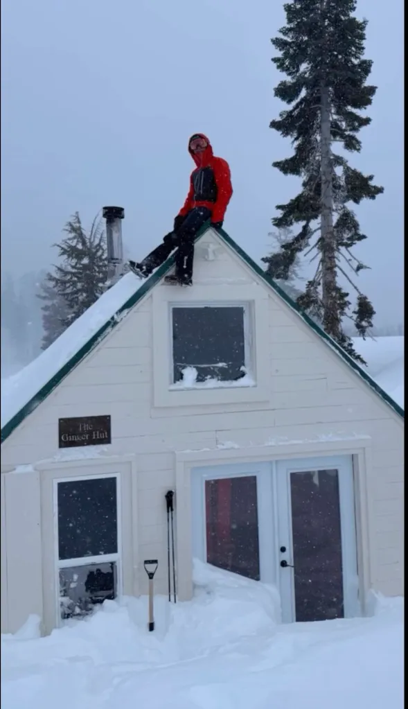 A person sitting on the peak of a snowy white cabin called 